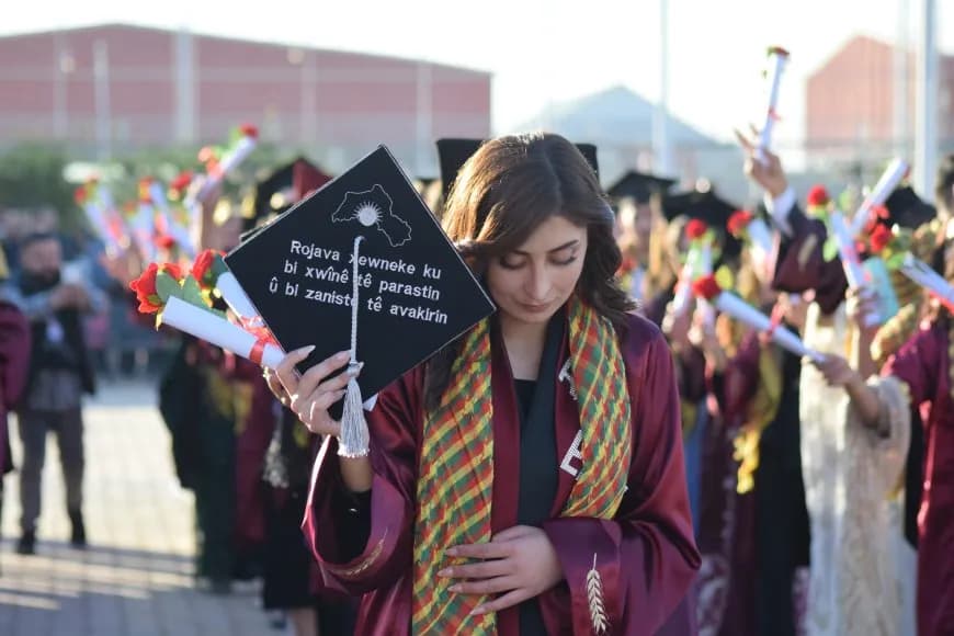 A graduate from Rojava University holding her graduation cap written on it, "Rojava is a dream that is defended by blood and established by science." Photo: ANHA