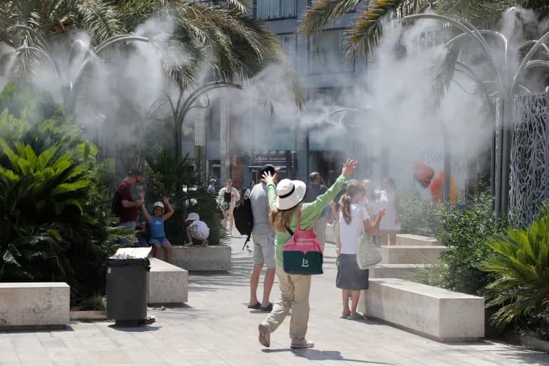 سياح يبردون أجسامهم برذاذ المياه في ساحة الملكة بمدينة فالنسيا الإسبانية خلال موجة الحر