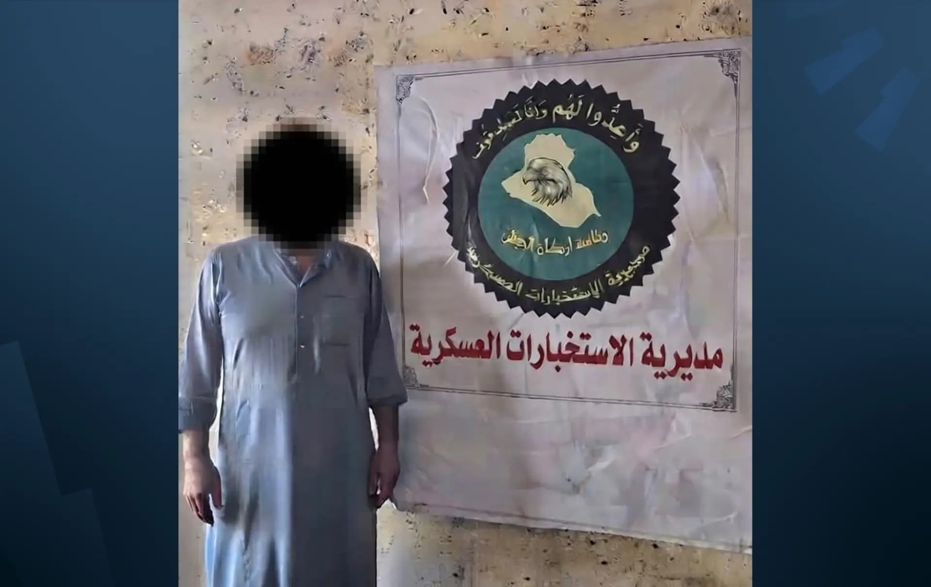ئەبو ساهیر لە بەردەم لۆگۆی دەزگای هەواڵگریی عێراق