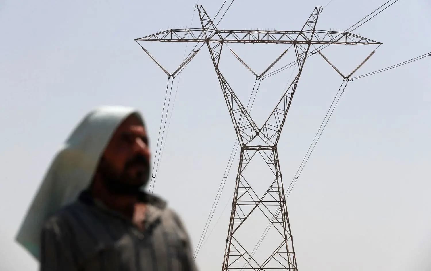 An Iraqi man stands under an electricity transmission tower south of Hilla city on August 10, 2025, amidst rising temperatures, chronic water shortages, and power cuts. Photo: Ahmad al-Rubaye/AFP
