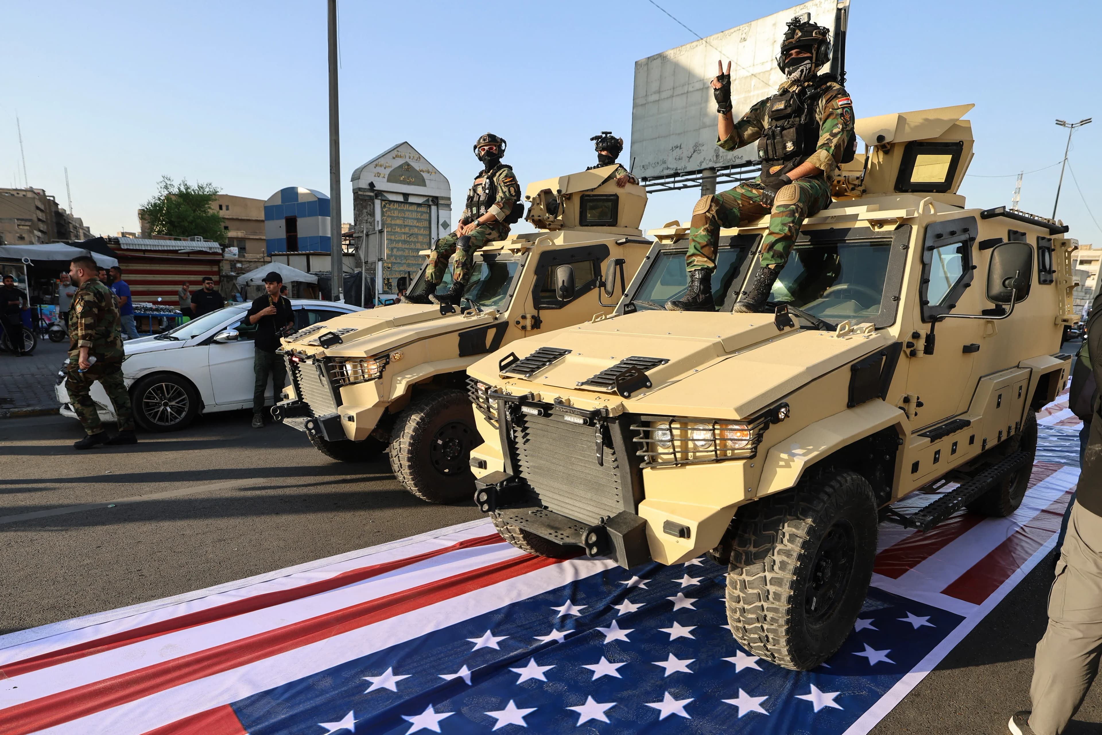 عناصر من الحشد الشعبي يمرّون بمركباتهم فوق علم أميركي خلال مراسم تشييع رمزية في بغداد-AFP